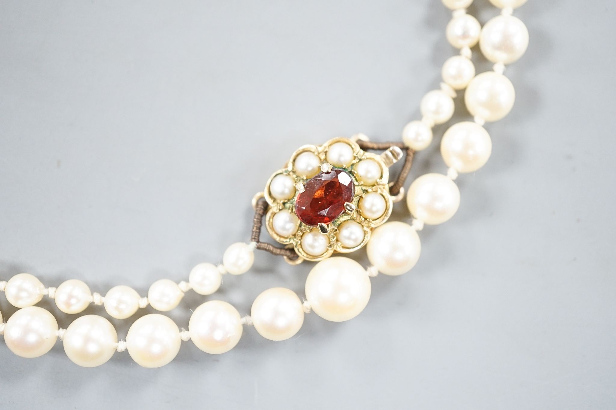 A single strand graduated cultured pearl necklace, with 9ct, garnet and cultured pearl cluster set clasp, 53cm.